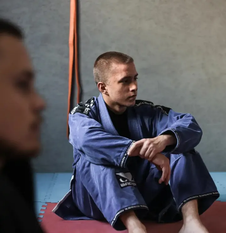 Zawodnik BJJ w niebieskim kimonie siedzi na macie